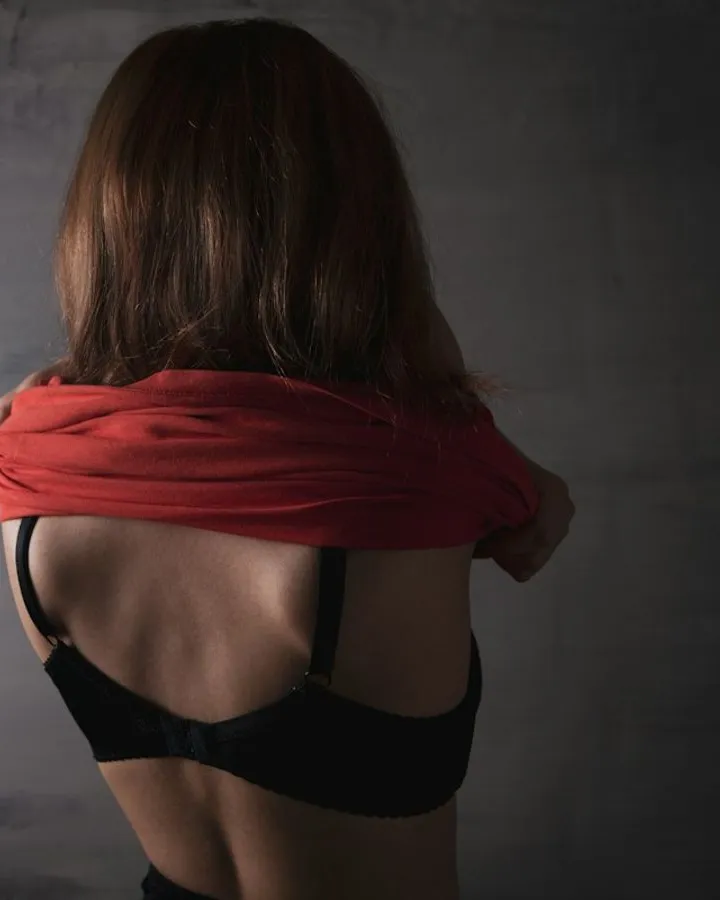 A woman taking off her red shirt, seen from behind